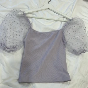 Ljuslila topp med puffärmar från Amisu - Säljer en superfin ljuslila topp från Amisu. Den har puffiga, genomskinliga ärmar med små prickar som ger en söt och unik look. Toppen är tight och perfekt för både vardag och fest. Tillverkad i Turkiet.