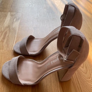 Beige klackskor - Säljer ett par snygga beige klackskor. De har en stilren design med öppen tå och en bred rem över foten. Skorna är gjorda i mocka och har en bekväm klack som ger bra stöd. Perfekta för både fest och vardag!