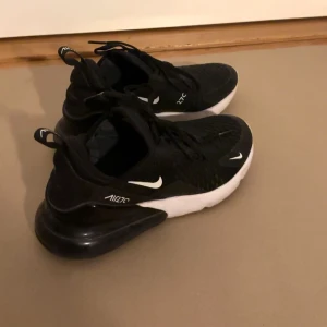Svarta Nike Air Max 270 - Säljer ett par snygga och bekväma svarta Nike Air Max 270 sneakers. De har en modern design med vit sula och den ikoniska Air Max-dämpningen i hälen. Perfekta för både vardag och träning. Skorna har snörning och är i bra skick.