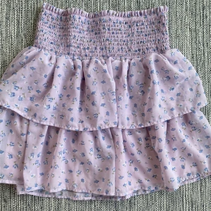 Lila volangkjol med blommor i strl S från Bubbleroom - Lila volangkjol med blommor i strl S från Bubbleroom.  Kjolen har en underkjol.  Sparsamt använd och i fint begagnat skick.  Mått Midjan: ca 34 cm Totallängd: ca 46 cm  Polyester  Kommer från ett djur och rökfritt hem.