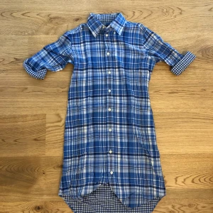 Blårutig skjortklänning från Ralph Lauren - Blå-vitrutig skjortklänning från Polo, Ralph Lauren. Storlek XS. Plagget är i gott skick. Finns en liten mörk fläck nedtill på baksidan. Den syns dock bara på mycket nära håll.