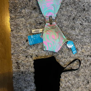 Färgglad bikini med mönster - Säljer en superfin bikini från Censor i storlek M. Överdelen har ett coolt mönster i rosa, grönt och blått med en snygg knytning framtill. Perfekt för sommarens alla badäventyr! den andra är en stilren svart bikini topp!