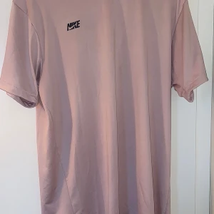 ROSA TRÖJA FRÅN NIKE - <br /> Den här Nike-tröjan är designad i en elegant rosa färg, vilket ger en modern och fräsch touch till vilken outfit som helst. Tillverkad av ett svalt och tunt tyg, erbjuder den en lätt och bekväm känsla, idealisk för varma klimat. 0763363570