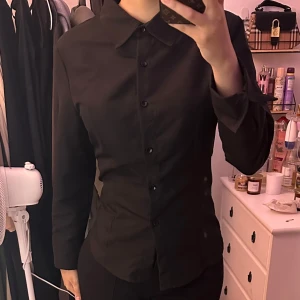 Shein svart skjorta med snören baktill - Jättefin och elegant svart skjorta från Shein som är slutsåld på hemsidan. Snören finns där bak som gör att man kan justera den runt midjan. Ger jättefin hourglass figur.