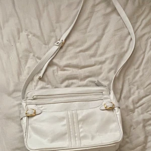 Vit axel väska - Den är vit med guld detaljer och justerbart band med många fickor. Jag har knappast använt den så den är i bra skick, och tyvärr vet jag inte märket
