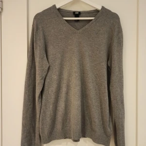Grå tröja från H&M - Säljer en stilren grå tröja från H&M i storlek M. Tröjan är tillverkad av 80% bomull och 20% polyester, vilket gör den både bekväm och hållbar. Den har en klassisk v-ringning och långa ärmar, perfekt för vardag under höst och vinter🌟