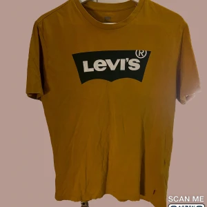 Gul t-shirt från Levi's - Säljer en snygg gul t-shirt från Levi's med deras ikoniska logga tryckt på bröstet. Perfekt för en avslappnad stil och passar till nästan allt. T-shirten är kortärmad och gjord i mjukt bomullsmaterial.