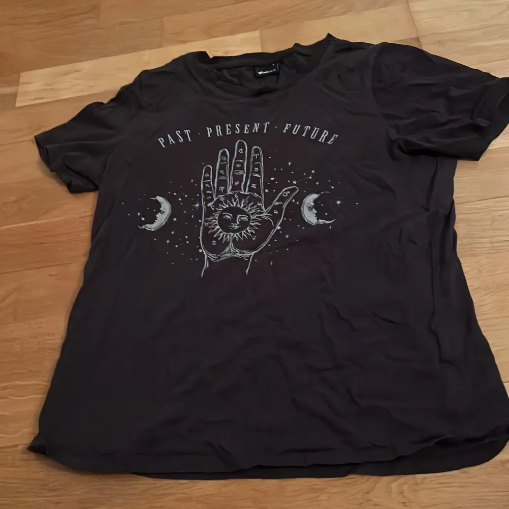 Säljer en svart t-shirt med ett coolt tryck av en hand med astrologiska symboler och texten 'Past Present Future'. T-shirten är kortärmad. . T-shirts.