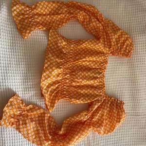 Orange blommig topp - Säljer en superfin orange topp med vita blommor. Den har korta puffärmar och en smickrande tight passform. Perfekt för sommardagar eller en festlig kväll. Toppen är i nyskick och redo för nya äventyr!
