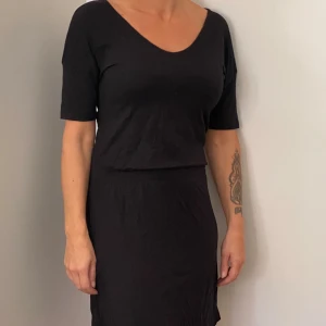 Svart klänning från 157 - Säljer en stilren svart klänning från 157 i storlek XS. Klänningen har en v-ringad hals och korta ärmar, perfekt för både vardag och fest. Materialet är mjukt och bekvämt, vilket gör den lätt att bära hela dagen. Passformen är normal och den är i nyskick.