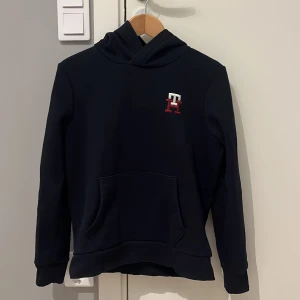 Svart hoodie från Tommy Hilfiger - Säljer en stilren svart hoodie från Tommy Hilfiger i storlek 164. Tröjan är i toppen skick och använd ett fåtal gånger. Skriv vid funderingar!