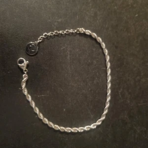 Silverfärgat armband med tvinnad design - Snyggt silverfärgat armband med en tvinnad design som ger en elegant touch, från Edblad. Längd ca 16-19cm 