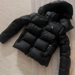 Calvin Klein Jacka - Säljer denna jacka då jag köpt ny, har använt den en hel vinter. Nypris: 2699kr och det låga priset beror på två hål som en skräddare sytt ihop, som syns på bild 3,4. Den glansiga pricken på bild 4 är ett lim skräddaren använt😊skriv för fler bilder