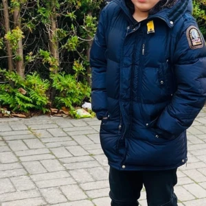 Mörkblå parkajacka från Parajumpers - Säljer en snygg och varm mörkblå parkajacka från Parajumpers. Jackan har en huva och är dekorerad med ett märke på ärmen. Den har dragkedja och knappar framtill för extra skydd mot kylan. Perfekt för vintern! ❄️