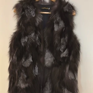 Pälsväst - Snygg väst i äkta päls,  i mörkt grått med silverfärgade detaljer. Västen är i fint skick, oanvänd och har en snygg passform. Oanvänd. 