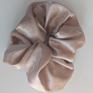 Beige scrunchie i satin - Säljer en superfin beige scrunchie i satin. Den är perfekt för att ge en lyxig touch till vilken frisyr som helst. Materialet är mjukt och glansigt, vilket gör den både snygg och skonsam mot håret. Perfekt accessoar för både vardag och fest!