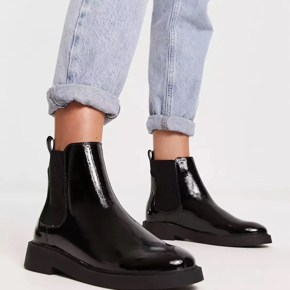 Ett par snygga svarta blanka boots i skinn. De har en stilren design med elastiska paneler på sidorna för enkel på- och avtagning. Perfekta för både vardag och fest!. Kengät.