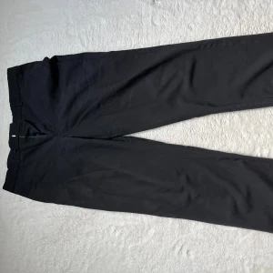 Svarta kostymbyxor från Batistini - Säljer ett par stiliga svarta kostymbyxor från Batistini. De har en klassisk design med raka ben och en knappdetalj på bakfickan. Perfekta för både formella tillfällen och kontoret. Byxorna är i bra skick och redo för en ny ägare! Är 180 och väger 75