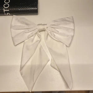 Vit diadem med stor rosett - Elegant vitt diadem med en stor rosett, perfekt för att ge en stilfull touch till din outfit. Rosetten är i ett mjukt material som ger en lyxig känsla.