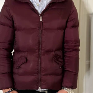 Vinröd pufferjacka från GANT  - Säljer en snygg vinröd pufferjacka från GANT. Jackan har en dragkedja framtill och praktiska fickor. Perfekt för vintern. Jag säljer den för den är för liten och har växt ur den. Den är tidigare köpt här på Plick därav de låga priset.  Ny pris på jackan är 3200. Den har inga skador och sitter lite kort. 