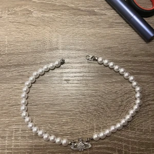 Pärlhalsband med silverdetalj - Elegant pärlhalsband med vita pärlor och en unik silverdetalj i mitten. Perfekt för att ge en klassisk touch till din outfit.