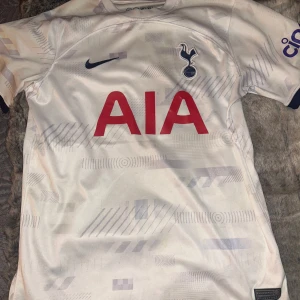 Totenhamn tröja Vit fotbollströja från Nike  - Säljer en vit fotbollströja från Nike med korta ärmar. Tröjan har ett subtilt mönster och klubbens logga på bröstet. Den har även en röd sponsorlogga på framsidan.