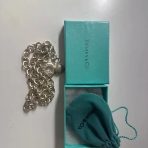 Silverhalsband från Tiffany & Co. - Elegant silverhalsband från Tiffany & Co. med ett hjärtformat hänge och en snäckdetalj. Halsbandet kommer i den ikoniska turkosa förpackningen med en matchande tygpåse.