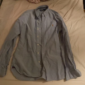 Blå skjorta från Polo Ralph Lauren - Säljer en stilren blå skjorta med det nya märket från Polo Ralph Lauren i slim fit. Skjortan är size S och modellen på bilden är 175. Vid fler frågor eller funderingar är det bara att skriva!