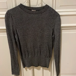 Glittrig grå tröja - Snygg glittrig grå tröja med långa ärmar och ribbad kant vid hals och midja. Perfekt för att lysa upp vilken outfit som helst. Passar bra till både vardag och festliga tillfällen.