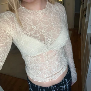 Vit spetsblus - Säljer en elegant vit spetsblus med långärmad design. Blusen är genomskinlig och har en croppad passform, perfekt för en stilren look.