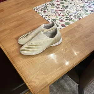 Beige fotbollsskor från Adidas - Säljer ett par stilrena beige fotbollsskor från Adidas. Skorna har en slät design med diskreta perforeringar och en vit sula. Perfekta för inomhusspel.