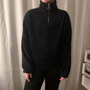 Svart fleece tröja från Chiquelle - Mysig svart fleece tröja från Chiquelle med dragkedja och hög krage. Perfekt för kyliga dagar!. Tröjan har en avslappnad passform och långa ärmar. Resår längst ner till midjan och längst ner i ärmarna.