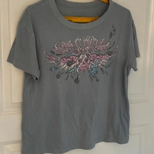 Grå Zadig & Voltaire  t-shirt med tryck - Snygg grå t-shirt med ett coolt tryck av en dödskalle och blommor på framsidan. På baksidan finns texten 'UNLIMITED LOVE TOUR' med en lista över städer. Perfekt för en avslappnad stil.