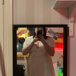 Vit omlottklänning - Säljer en elegant vit omlottklänning med knytband i midjan. Klänningen har en v-ringad design och korta ärmar, perfekt för sommarens festligheter. Bandet i midjan är inte fast sytt, tyvärr lite genomskinligt baktill