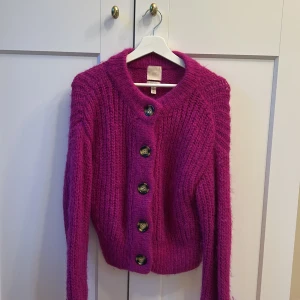 Rosa stickad kofta  - Säljer en mysig rosa stickad kofta från H&M i alpackablandning. Koftan har stora knappar och långa ärmar, perfekt för kyliga dagar. En härlig färgklick i garderoben!