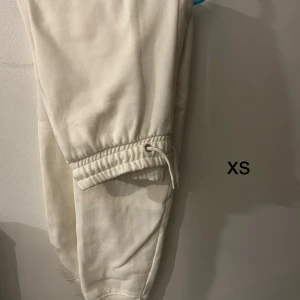 Beige mjukisbyxor i storlek XS - Säljer ett par bekväma beige mjukisbyxor i storlek XS. Byxorna har elastisk midja med snörning och muddar vid bensluten för en skön passform.