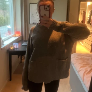 Grå stickad tröja - Mysig grå stickad tröja med långa ärmar och ribbstickade muddar. Perfekt för kyliga dagar. Tröjan har en avslappnad passform och praktiska fickor framtill.