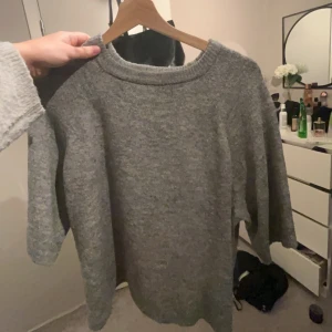 Grå stickad tröja - Mysig grå stickad tröja med rund halsringning och långa ärmar. Perfekt för kyliga dagar och enkel att matcha med olika outfits. 