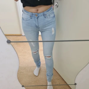 Ljusa jeans från Forever 21 strl 34 - Säljer ett par ljusa jeans från Forever 21 med slitna detaljer och en avslappnad look. De har en knapp och dragkedja framtill samt klassiska fem fickor. Säljer då de är för lite för mig.