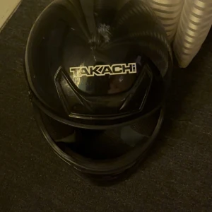 Svart moped hjälm från Takachi - Säljer en svart Takachi TK-30 hjälm den är använd ett bra tag men den funkar som en ska  . Den har en stilren design med justerbart spänne och ventilationsöppningar. Perfekt för motorcykelentusiaster som söker både säkerhet och stil. 