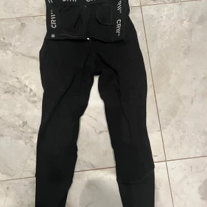 Ridbyxor från Hööks - Säljer ett par svarta ridbyxor från CRW med elastisk midja och knappstängning. Perfekta ridbyxor. Enkel design med CRW-logga på insidan av midjan. Innerlängd; 60 cm full byxlängd: 84 cm 