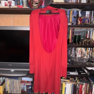 Röd långklänning med öppen rygg - Elegant röd långklänning med en djup öppen rygg och långa ärmar. Perfekt för en kväll ute eller en speciell tillställning. Klänningen har en smickrande passform och är tillverkad i ett mjukt material som ger ett vackert fall. Passar till Julfester 