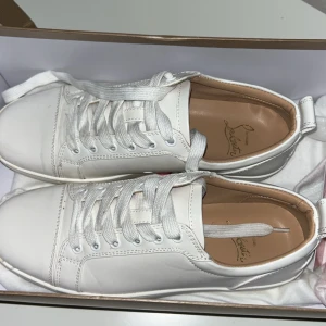  Christian Louboutin sneakers utan spikar - Snygga vita sneakers från Christian Louboutin med den ikoniska röda sulan. Skorna har snörning och är tillverkade i skinn, vilket ger en lyxig känsla. Perfekta för att ge din outfit en stilren touch. AI text haha men om det är något du undrar över så är det bara att skriva!🙌🏻