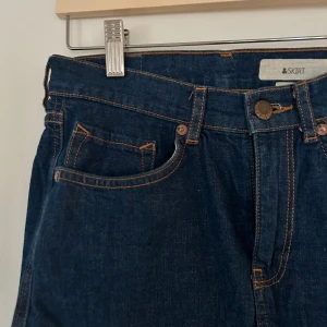 Mörkblå jeanskjol från &Skirt - Snygg mörkblå jeanskjol från &Skirt med klassisk femficksdesign Perfekt för en avslappnad stil med en t-shirt eller blus. Kjolen har en rak passform och är i en kort modell.