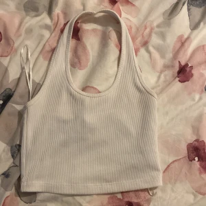 Vit ribbad linnetopp från H&M Divided - Säljer en stilren vit ribbad linnetopp från H&M Divided. Toppen har en rund halsringning och är ärmlös, perfekt för varma dagar. Den är enkel att matcha med olika outfits och ger en fräsch look.