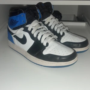 Nike Air Jordans i svart, vit och blå - Snygga Nike Air Jordans i en klassisk färgkombination av svart, vit och blå. Skorna har snörning och en hög design som ger bra stöd. Perfekta för både stil och komfort.