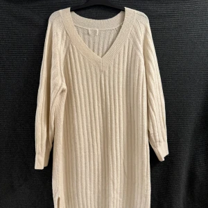 Beige ribbad klänning - Snygg beige ribbad klänning med v-ringning och långa ärmar. Klänningen har en slits på sidan som gör den lite extra elegant har använt två , tre gånger men är i bra skick 