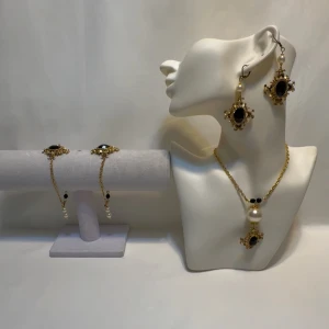 Elegant smyckesset med svarta stenar och pärlor svart  - Snyggt smyckesset med örhängen, halsband och armband i guldton. Setet har svarta stenar och vita pärlor som ger en lyxig känsla. Perfekt för att lyfta din outfit till nästa nivå.