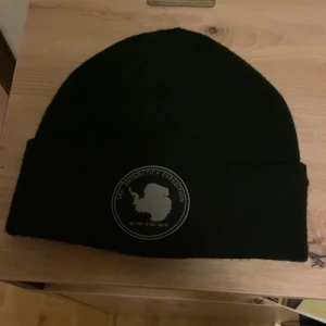 Svart mössa med Sail Antarctica Expedition-märke - Snygg svart mössa med ett coolt Sail Antarctica Expedition-märke framtill. Perfekt för kalla dagar och äventyr. Enkel och stilren design som passar till det mesta. Knappt använd