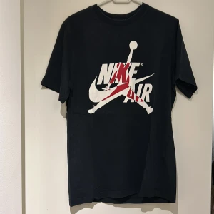 Svart Nike Air Jordan t-shirt - Snygg svart t-shirt från Nike med det ikoniska Air Jordan-trycket i vitt och rött på framsidan. Perfekt för alla som älskar streetwear och sportig stil. Kortärmad och tillverkad i mjukt material för maximal komfort.